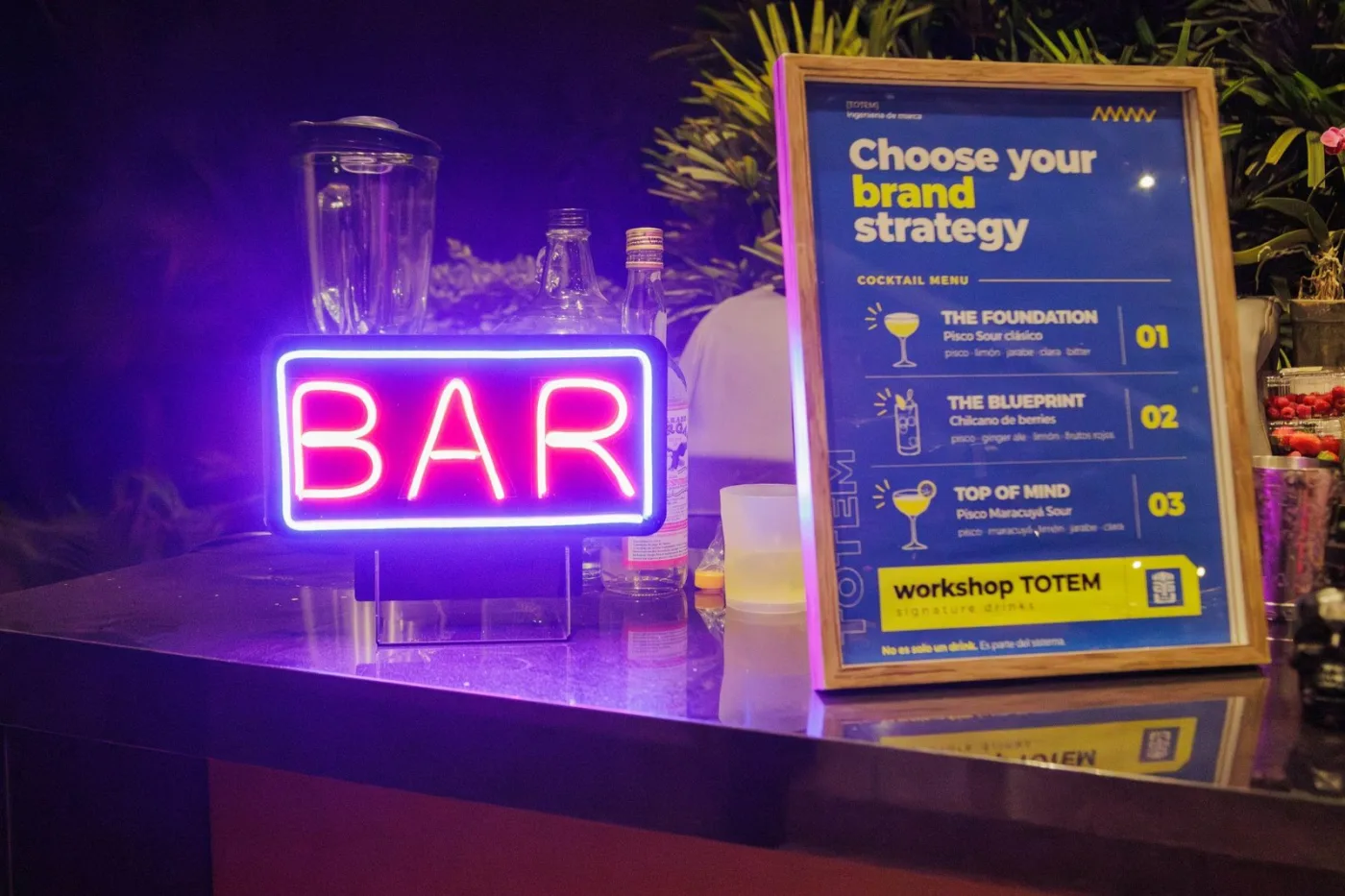 Barra del evento con letrero de neón «BAR» y la carta de tragos «Choose your brand strategy»