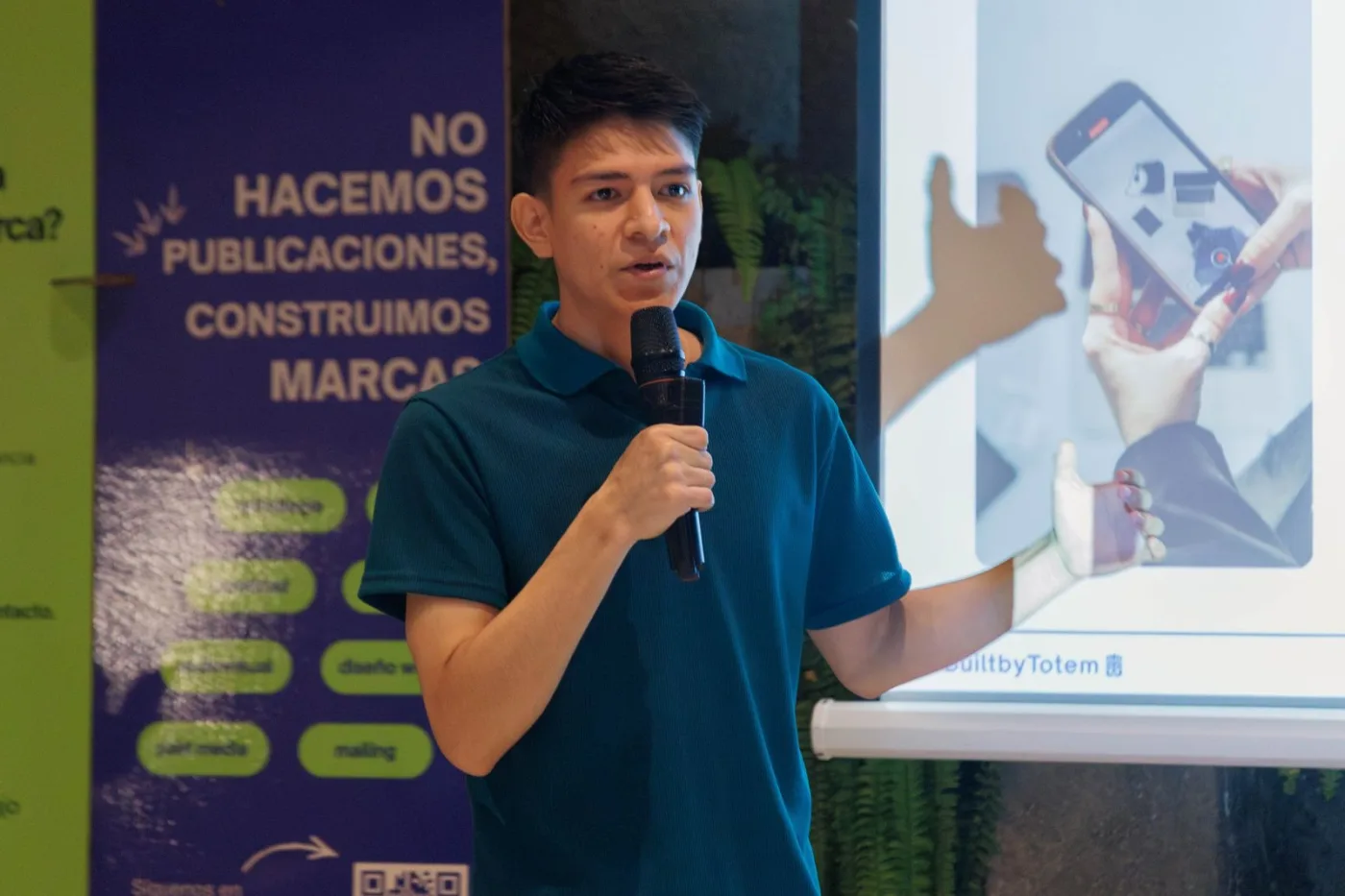 Expositor de TOTEM con micrófono frente al banner «No hacemos publicaciones, construimos marcas»